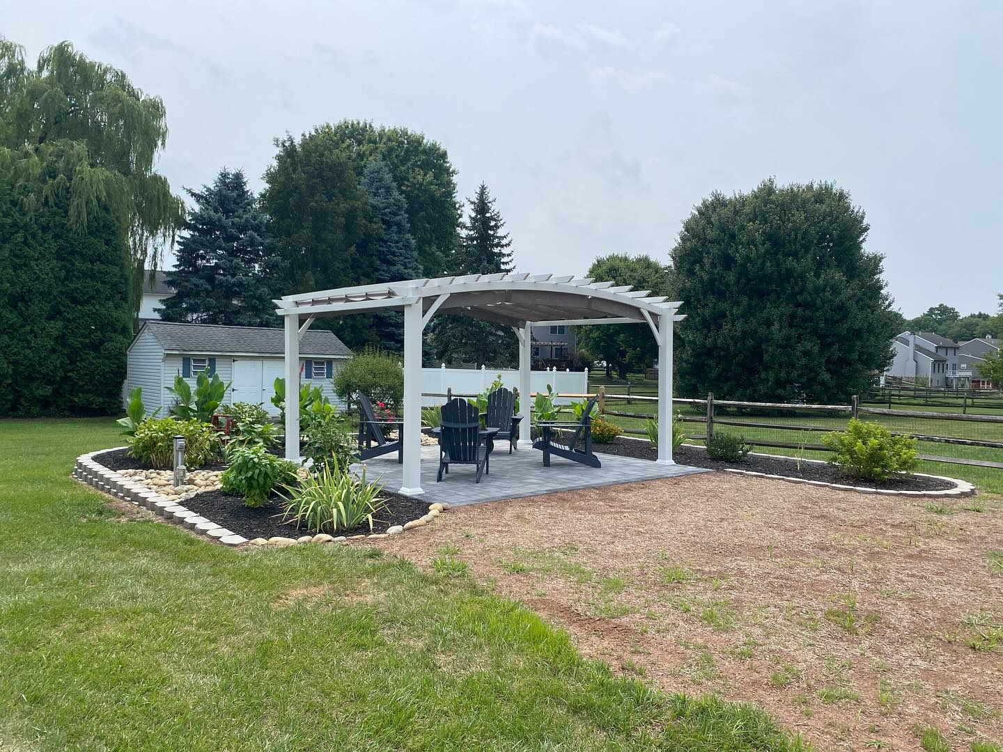 White pergola with patio seating, landscape beds, and decorative stone border in a backyard outdoor living space